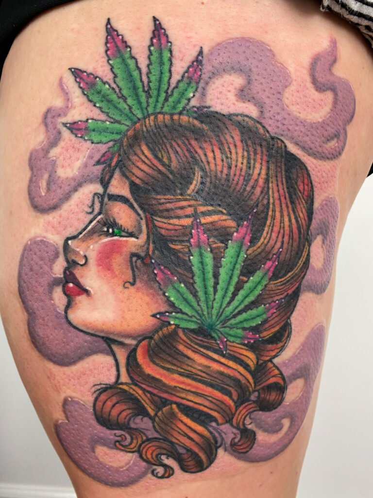 a neo traditional tattoo of a woman’s head surrounded by purple colored smoke and in her hair ate two pot leaves. The woman has a profile view. And bright red ink in her lips and green eyes. This tattoo was done by Jeremy Moffitt an artist at Near Me Tattoo located at 6721 Bells Ferry Rd Ste D110 Woodstock, Ga. 30189