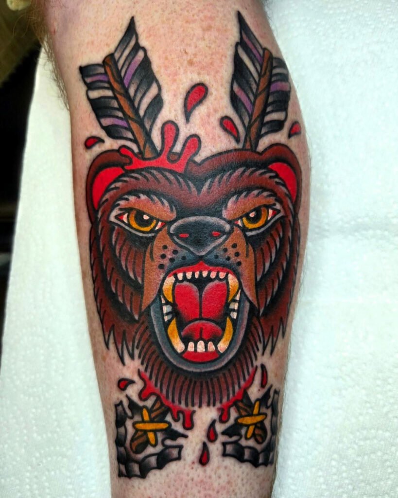 An American traditional bear head with arrows going through it. The bear is snarling angrily. The two crossed arrows have knapped arrow heads and purple and black feathers. This tattoo was made by Noah Beach, co owner of Near Me Tattoo at 6721 Bells Ferry Rd Ste D110 Woodstock, Ga. 30189