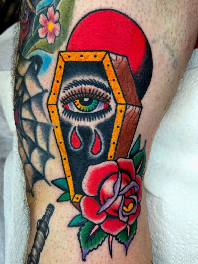 Neo traditional tattoo of a coffin with a large green and yellow colored eye peering from it. There is a blood red moon and rose added to the picture. This tattoo was made by Noah Beach, co owner of Near Me Tattoo at 6721 Bells Ferry Rd Ste D110 Woodstock, Ga. 30189