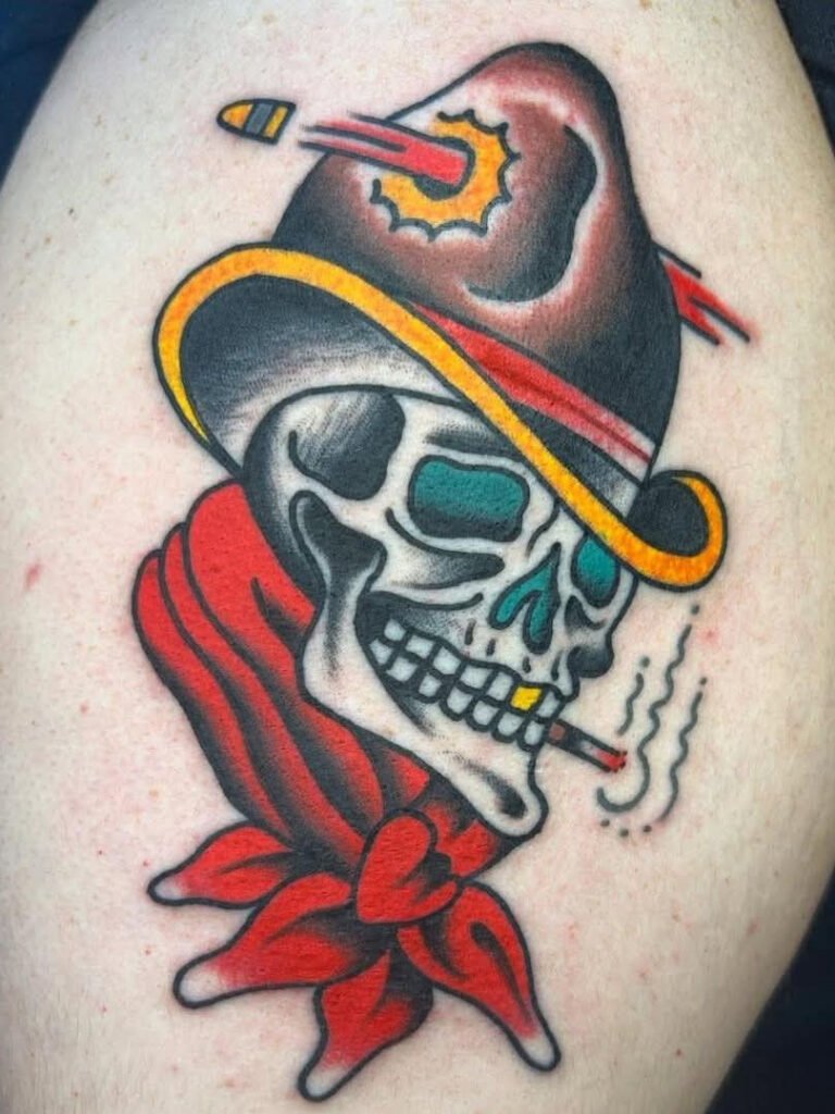 an American traditional rough rider tattoo. It depicts a skull with a red bandana and wearing a cowboy hat with a bullet piercing through the hat. The skull has a lit cigarette in its mouth. This tattoo was made by Noah Beach, co owner of Near Me Tattoo at 6721 Bells Ferry Rd Ste D110 Woodstock, Ga. 30189