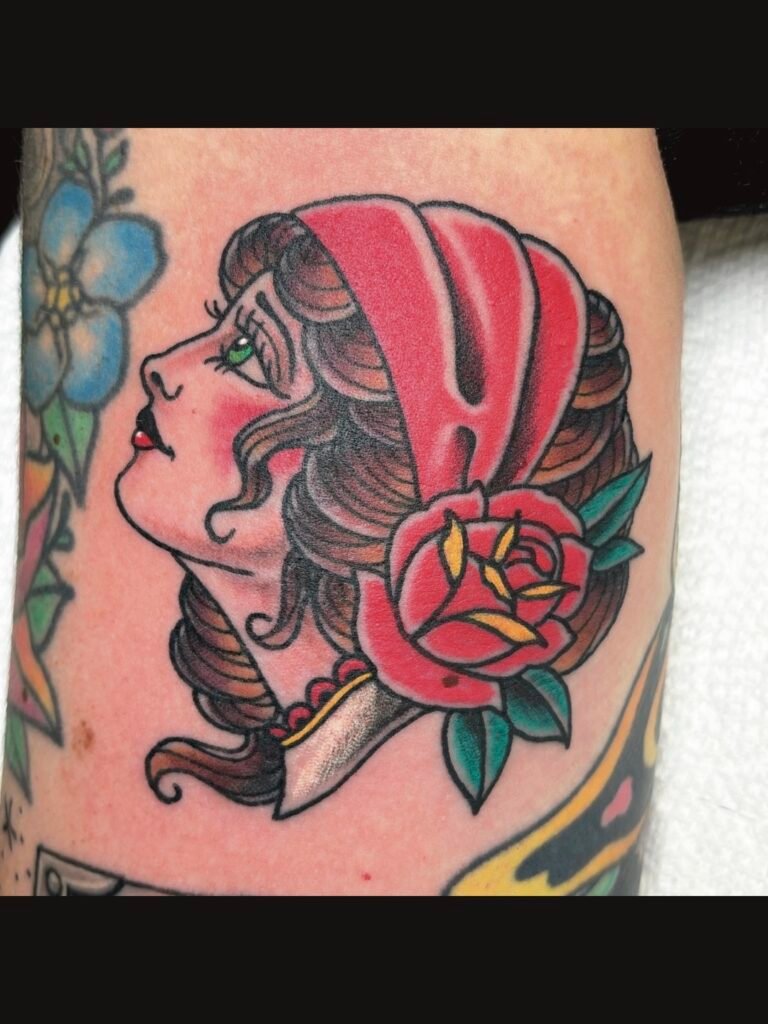 a Neo traditional take on the American traditional girl head, or gypsy head. The tattoo has the woman wearing a red bonnet with a red rose. This tattoo was done by Jeremy Moffitt an artist at Near Me Tattoo located at 6721 Bells Ferry Rd Ste D110 Woodstock, Ga. 30189