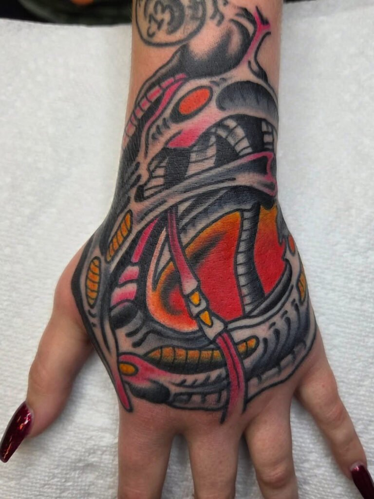 a biomech style tattoo on the hand. It has a grey and pink structures with yellow ribs moving in random flowing directions and a hot red and orange background. This tattoo was made by Noah Beach, co owner of Near Me Tattoo at 6721 Bells Ferry Rd Ste D110 Woodstock, Ga. 30189
