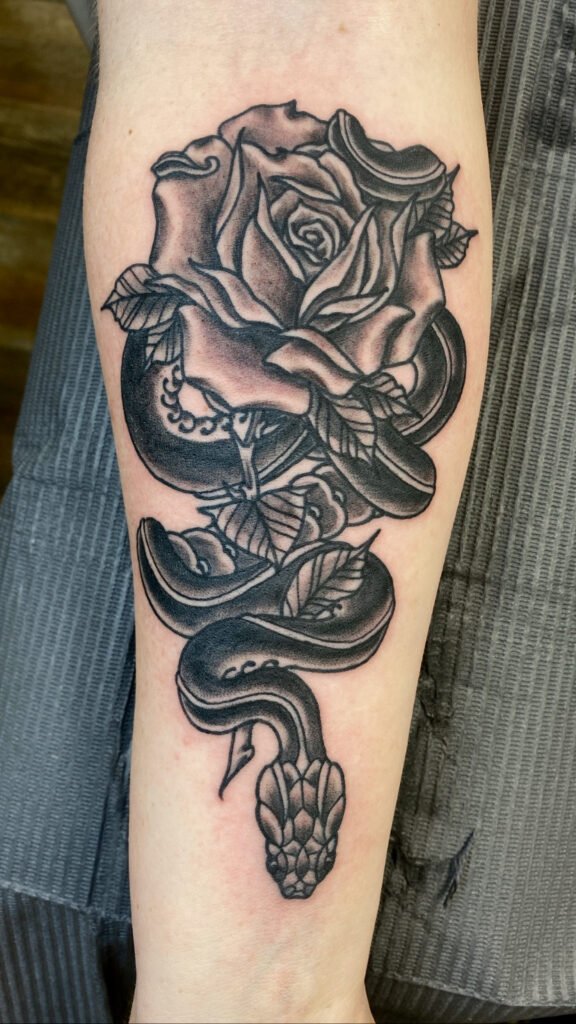 A black and grey tattoo of a snake descending down the wearers forearm towards the hand. To the top of the tattoo is the tail of the snake which is wrapped around a grey shaded rose. This tattoo was done by Jeremy Moffitt an artist at Near Me Tattoo located at 6721 Bells Ferry Rd Ste D110 Woodstock, Ga. 30189