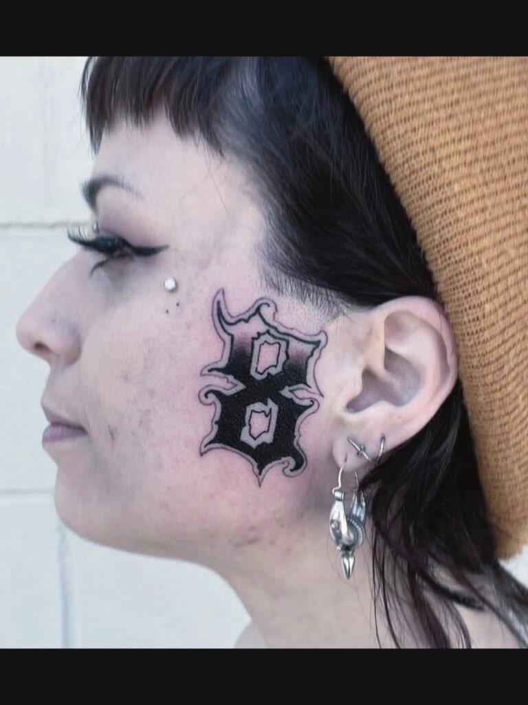 a Chicano style tattoo of the number 8 on the check area of a woman. It is done in black and grey with a ghost line border to create a halo. This tattoo was made by Noah Beach, co owner of Near Me Tattoo at 6721 Bells Ferry Rd Ste D110 Woodstock, Ga. 30189