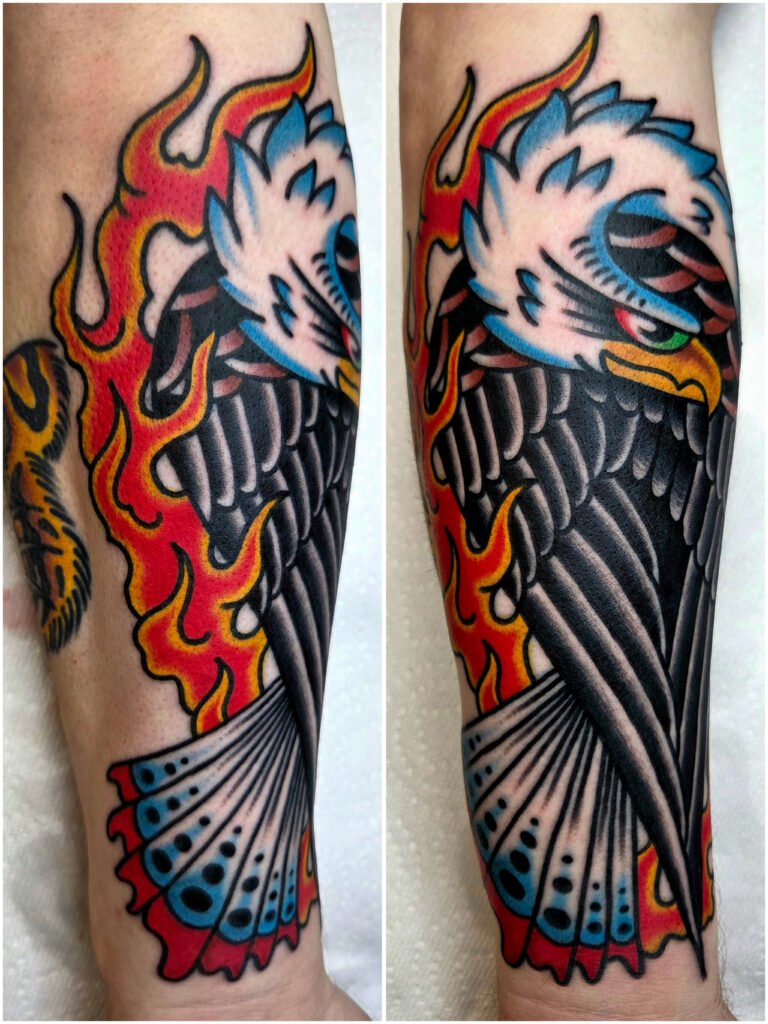 a Neo traditional American traditional eagle tattoo with flames reaching from behind and around the side and towards the eagles front. The view of the eagle is from the back with its wings tucked in and tips touching. The eagles head is turned around and looking to the right of the image. the eagles tail is tipped in red and has distinctive dot patterns on them. This tattoo was made by Noah Beach, co owner of Near Me Tattoo at 6721 Bells Ferry Rd Ste D110 Woodstock, Ga. 30189