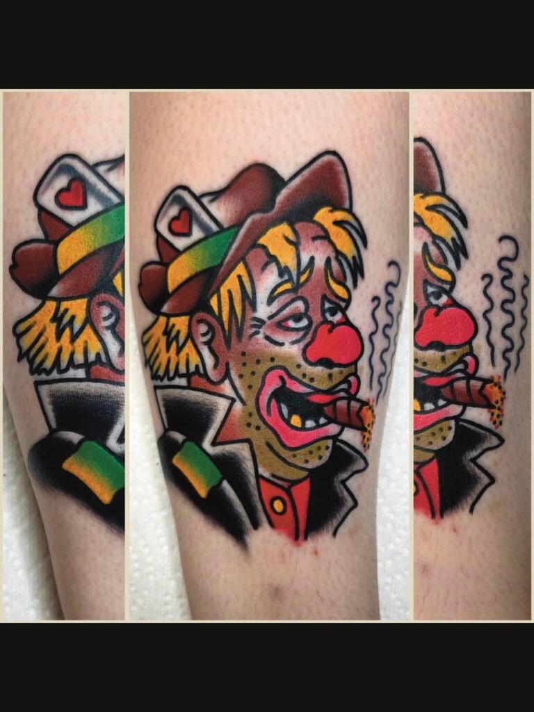 Neo Traditional tattoo of a hobo with a cigar. It is a spin on the traditional tramp cartoon tattoo. The tramp has blond hair peaking out under a fedora with a card with a heart in it. he has a happy drunken face with a red nose and gold tooth in his grin. The cigar has a glowing tip and his suit jacket is patched with a green patch. This tattoo was made by Noah Beach, co owner of Near Me Tattoo at 6721 Bells Ferry Rd Ste D110 Woodstock, Ga. 30189
