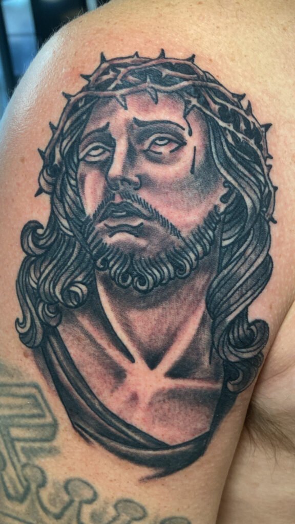 An American traditional Jesus tattoo. It shows Christ with a crown of thorns looking up. It is traditionally shaded. This tattoo was done by Jeremy Moffitt an artist at Near Me Tattoo located at 6721 Bells Ferry Rd Ste D110 Woodstock, Ga. 30189