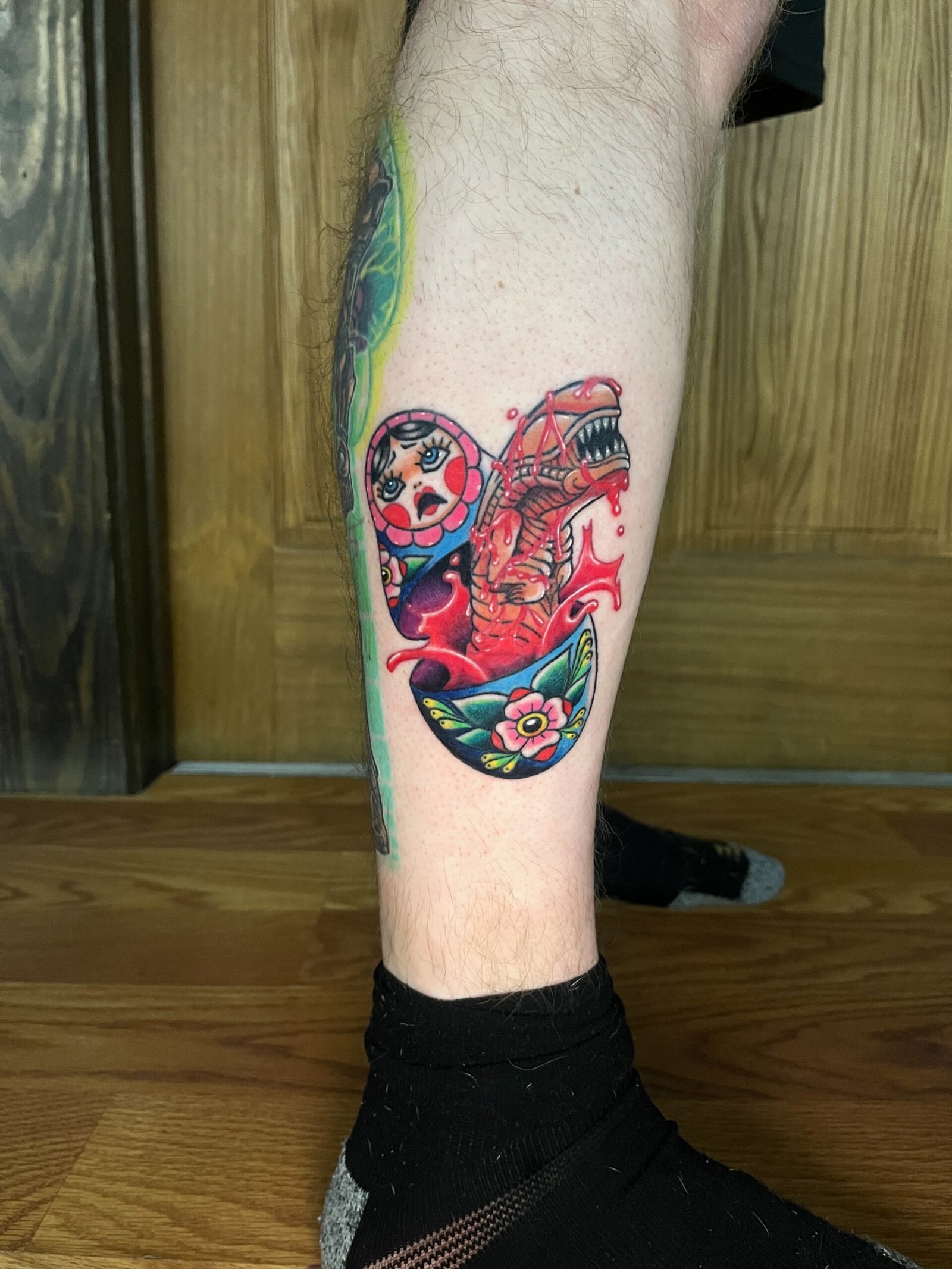 A Neo traditional tattoo mashup tattoo of an alien Xenomorph chestburster popping out of a Russian nesting doll. There is blood colored liquid bursting all around from the inside of the doll and the doll has a shocked look on its face. View 2 This tattoo was made by Dani Lopez, a tattoo artist at Near Me Tattoo at 6721 Bells Ferry Rd. Ste D110 Woodstock, Ga 30189