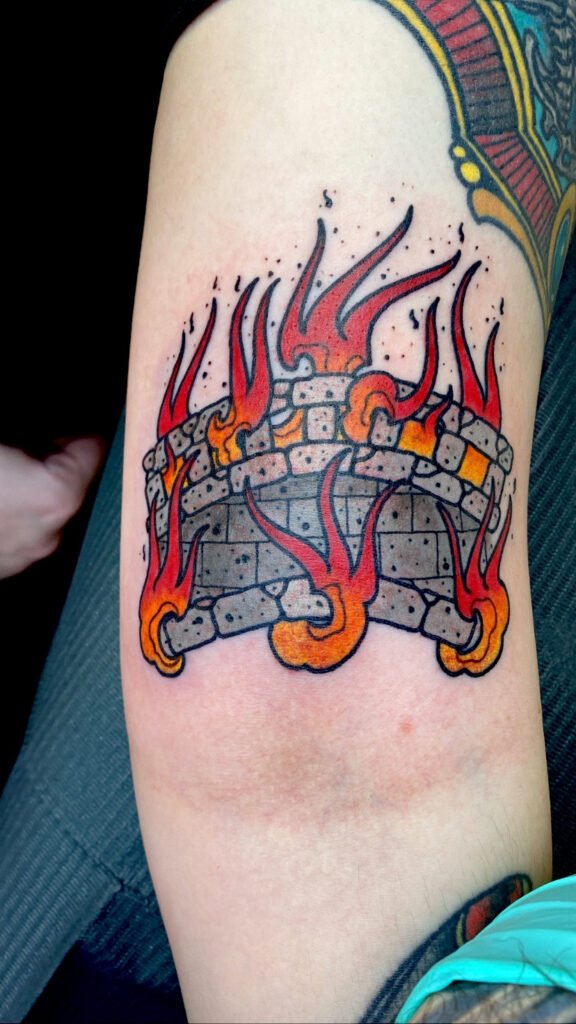 A Neo traditional tattoo of a burning bridge. The bridge is made of stone brick and is engulfed in orange and red fire. It is a take on the phrase dont burn your bridges or may the bridges i burn light the way. This tattoo was done by Jeremy Moffitt an artist at Near Me Tattoo located at 6721 Bells Ferry Rd Ste D110 Woodstock, Ga. 30189