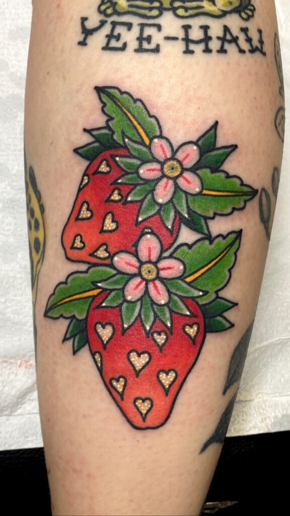 a Neo traditional tattoo of two strawberries. The normal white seeds are replaced by glitter ink hearts making for a cute and sparkly looking tattoo. This tattoo was done by Jeremy Moffitt an artist at Near Me Tattoo located at 6721 Bells Ferry Rd Ste D110 Woodstock, Ga. 30189