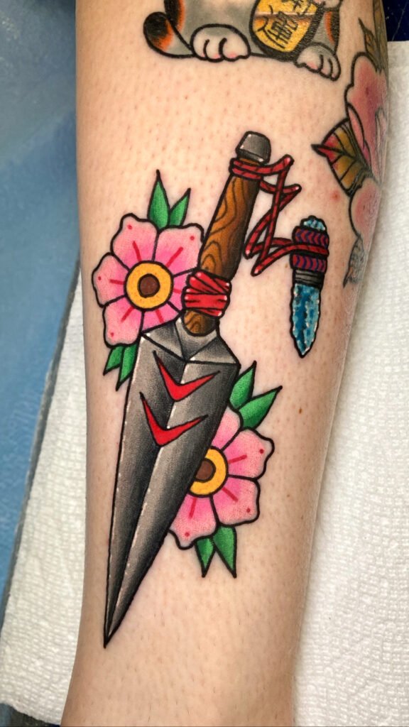 A neo Japanese style tattoo of a Kunai and sakura or cherry blossom flowers. It has a a crystal with distinctive blue ink attached to the throwing knife. This tattoo was done by Jeremy Moffitt an artist at Near Me Tattoo located at 6721 Bells Ferry Rd Ste D110 Woodstock, Ga. 30189