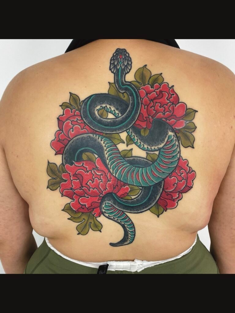 a neo Japanese traditional tattoo of a snake and 4 peonies taking up the entire upper back of a woman. The peonies are done in two tone red ink. And the snake is black with teal accenting. This tattoo was done by Jeremy Moffitt an artist at Near Me Tattoo located at 6721 Bells Ferry Rd Ste D110 Woodstock, Ga. 30189