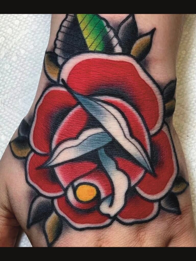 a Neo traditional take on an American traditional rose tattoo on the top of a persons hand. The bulk of the rose is done in red ink and it has a yellow center. The upturned leaves are white. And the leaves are deep green with one special leaf done in a bright green. This tattoo was made by Noah Beach, co owner of Near Me Tattoo at 6721 Bells Ferry Rd Ste D110 Woodstock, Ga. 30189