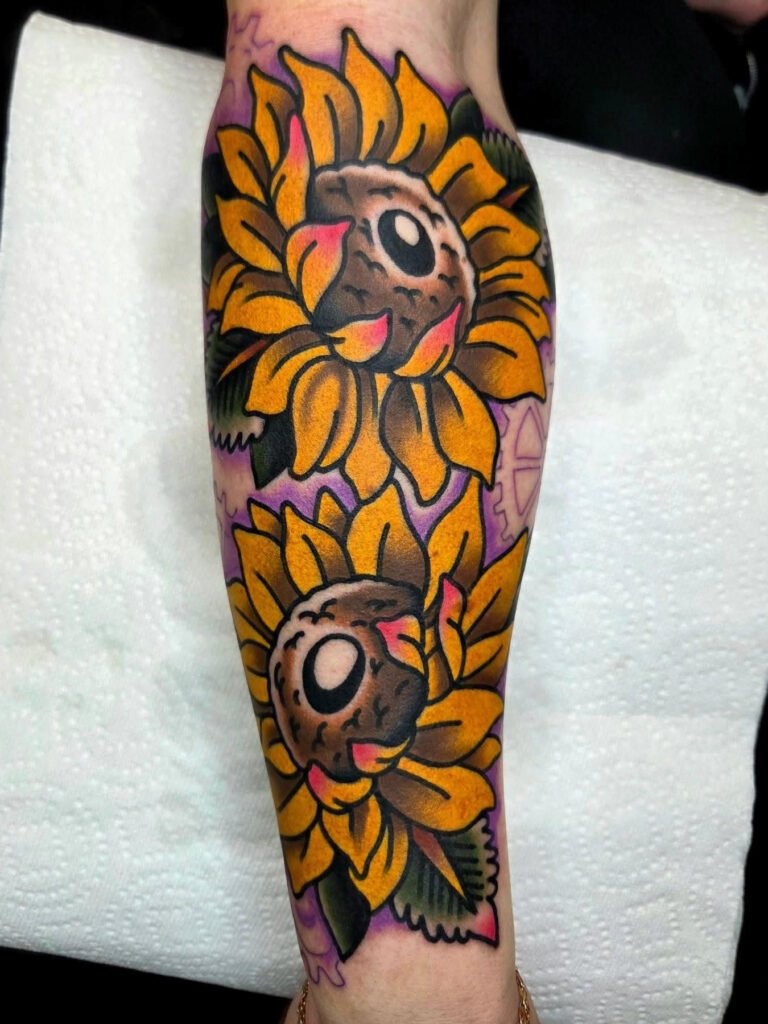 A large neo traditional tattoo of two sunflowers. They are large and are very striking due to the color palette of bright yellow for the petals and a bright purple background. This tattoo was made by Noah Beach, co owner of Near Me Tattoo at 6721 Bells Ferry Rd Ste D110 Woodstock, Ga. 30189