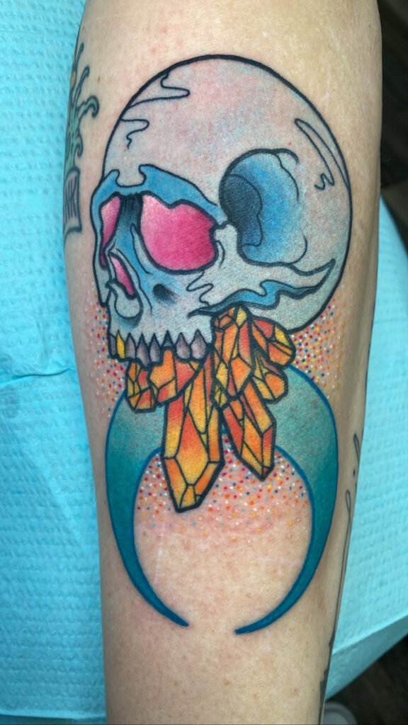 A Neo traditional tattoo of a skull with crystals coming out of its jaw and a crescent moon below that. The skull has glowing magenta colored eyes. The background also has a glitter ink effect giving the entire tattoo a colorful and vibrant aura. This tattoo was done by Jeremy Moffitt an artist at Near Me Tattoo located at 6721 Bells Ferry Rd Ste D110 Woodstock, Ga. 30189