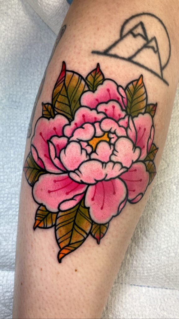 a neo traditional Japanese style peony flower tattoo. It has very well balanced colored ink with a pink pedals with red accents and a yellow center with olive colored leaves and warm colored tips. This tattoo was done by Jeremy Moffitt an artist at Near Me Tattoo located at 6721 Bells Ferry Rd Ste D110 Woodstock, Ga. 30189