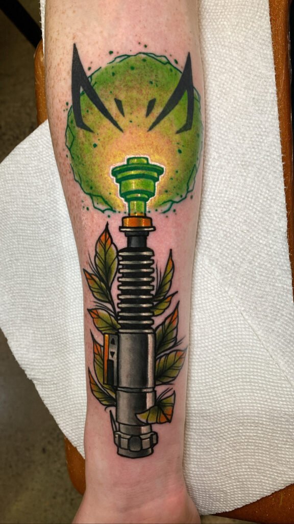 A Neo traditional tattoo of the light saber of Luke Skywalker. It is glowing green about to ignite. In the glow of the light saber turning on is a rebel symbol. This tattoo was done by Jeremy Moffitt an artist at Near Me Tattoo located at 6721 Bells Ferry Rd Ste D110 Woodstock, Ga. 30189