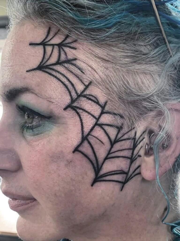 a tattoo of a woman with a spider web going from the top of her jaw to forehead. The tattoo has bold and fine lines. The face tattoo is cleanly and crisply done. This tattoo was made by Noah Beach, co owner of Near Me Tattoo at 6721 Bells Ferry Rd Ste D110 Woodstock, Ga. 30189