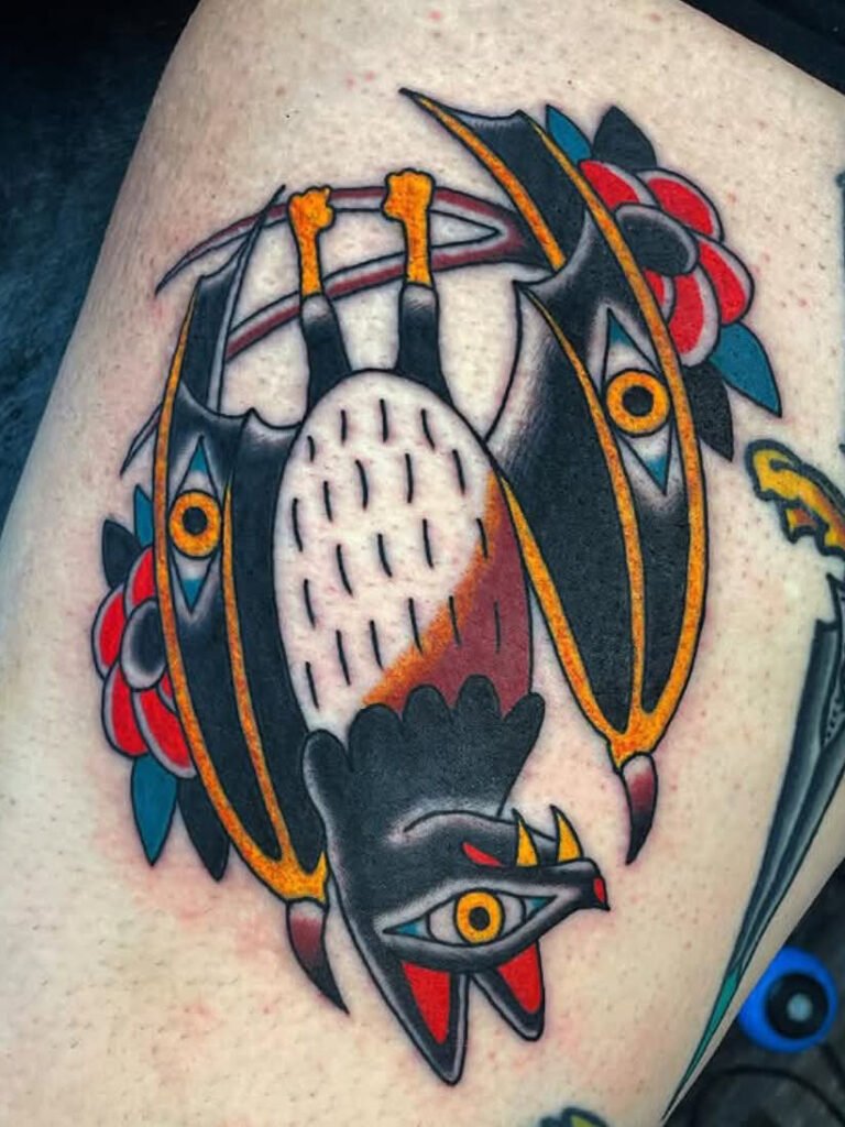 A Spanish traditional tattoo of an upside down bat. It has eyes in its wings and red poppy flowers behind its wings. Its claws are gripped to a branch and its white belly is exposed. This tattoo was made by Noah Beach, co owner of Near Me Tattoo at 6721 Bells Ferry Rd Ste D110 Woodstock, Ga. 30189