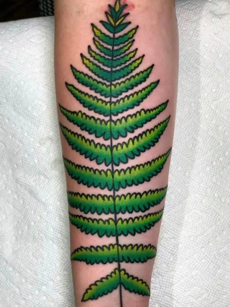 a traditional style tattoo of simple fern. It is a large tattoo taking up the back of the forearm and has a single line as its stem. The foliage is a middle green fading off into a yellow green. This tattoo was made by Noah Beach, co owner of Near Me Tattoo at 6721 Bells Ferry Rd Ste D110 Woodstock, Ga. 30189
