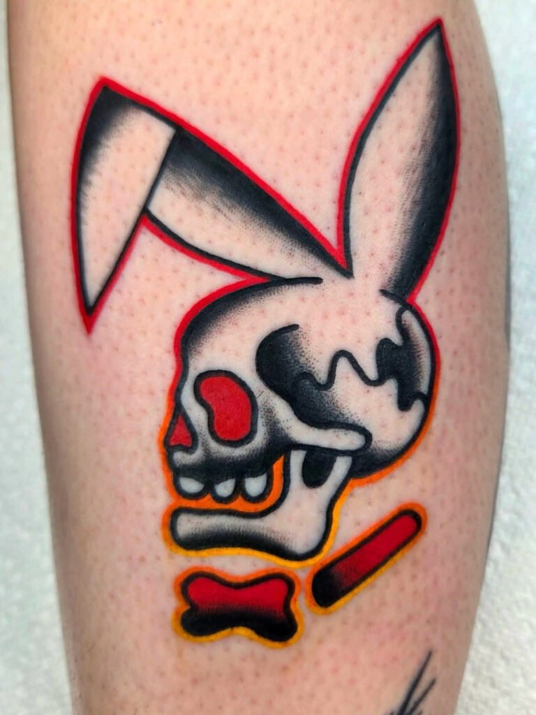 a Neo traditional style tattoo of a playboy bunny logo but replaced with a skull and ears in the same shape. It has a red bow tie and is halo outlined with a deep red color that fades to yellow as it descends the entire tattoo. This tattoo was made by Noah Beach, co owner of Near Me Tattoo at 6721 Bells Ferry Rd Ste D110 Woodstock, Ga. 30189