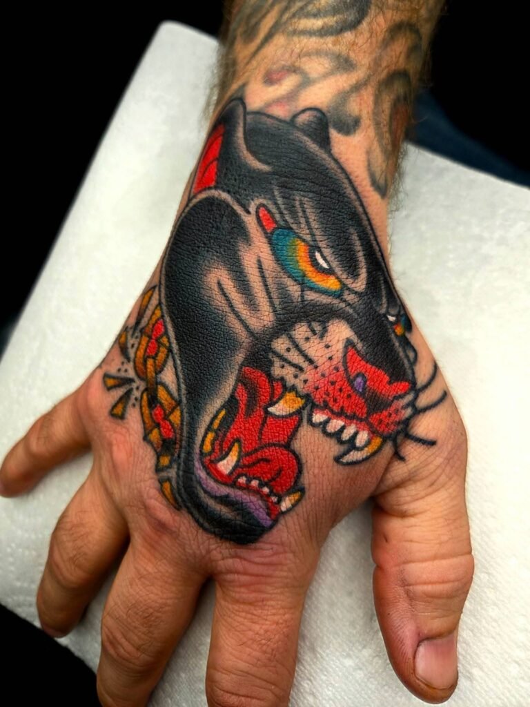 A tattoo of a snarling panther head on the back of the hand just above the finger. The Panther is done with black ink with a powerful color palette of bright complementary colors. It is a popular tattoo for men. This tattoo was done by Noah Beach co owner of Near Me Tattoo which is located at 6721 Bells Ferry Rd STE D110 Woodstock Georgia 30189