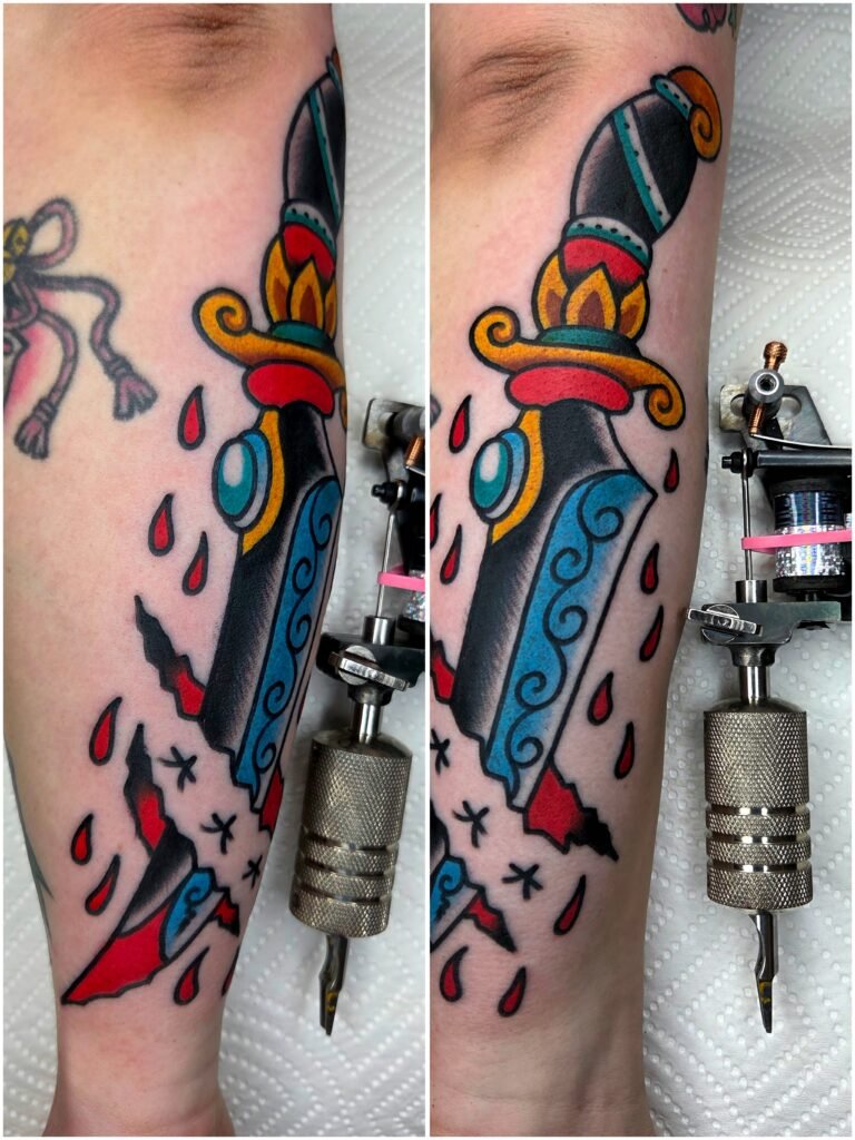 A Neo traditional tattoo of a dagger on the forearm of the wearer above the wrist hand and finger. It is done with heavily contrasting colored ink that gives it a striking appearance. Around it are red blood drops. The dagger design is also part of a skin rip that is made to look like it is going through the skin. This tattoo was done by Noah Beach co owner of Near Me Tattoo which is located at 6721 Bells Ferry Rd STE D110 Woodstock, Ga. 30189
