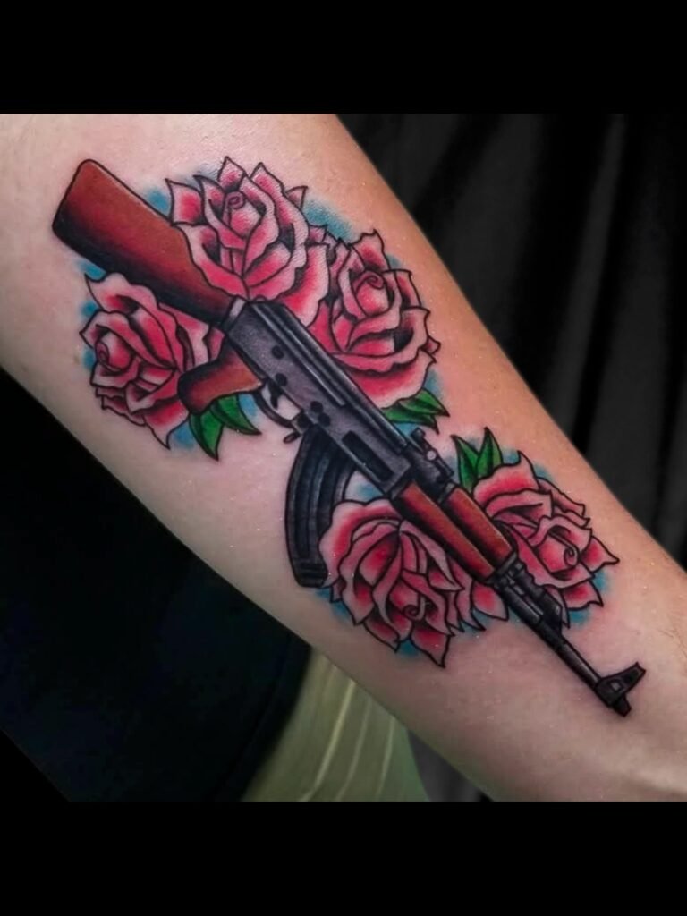 A tattoo of an Ak 47 type rifle laying on and among American traditional rose flowers. The ink is bright and contrasting in the leaves and background from the bright pinkish red of the pedals of the flowers. The Ak 47 has wooden furniture and is pointed towards the hand and finger of the arm of the wearer. This tattoo was made by Nathan Heinrich, co owner of Near Me Tattoo at 6721 Bells Ferry Rd Ste D110 Woodstock, Ga. 30189