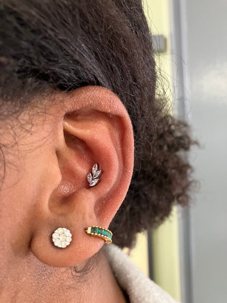 A picture of a conch ear piercing. It is very feminine in appearance and is popular for women to get. This jewelry was done with a base made of titanium. The topper is floral in appearance and resembles a fern made from four CZ oval shaped stones. This piercing was done by Hope Boyd the body piercer at Near Me Tattoo at 6721 Bells Ferry Rd STE D110 Woodstock, Georgia 30189