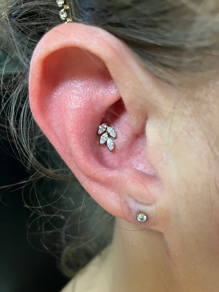 A photograph of a conch piercing. It is a very popular and beautiful ear piercing for men and women to receive. The jewelry used has a base of titanium and the topper is made to look floral using four oval shopped CZ stones. This piercing was done by Hope Boyd the body piercer at Near Me Tattoo at 6721 Bells Ferry Rd STE D110 Woodstock, Georgia 30189