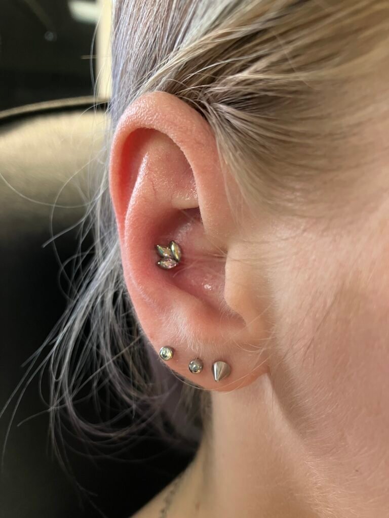 A photograph of a conch piercing done on the ear of a woman. This is one of the most popular for men and women alike. The jewelry base is made of titanium and the topper is a beautiful cut leaf pattern with three facets of CZ stone. It is very elegant in appearance. This piercing was done by Hope Boyd the body piercer at Near Me Tattoo at 6721 Bells Ferry Rd STE D110 Woodstock, Georgia 30189