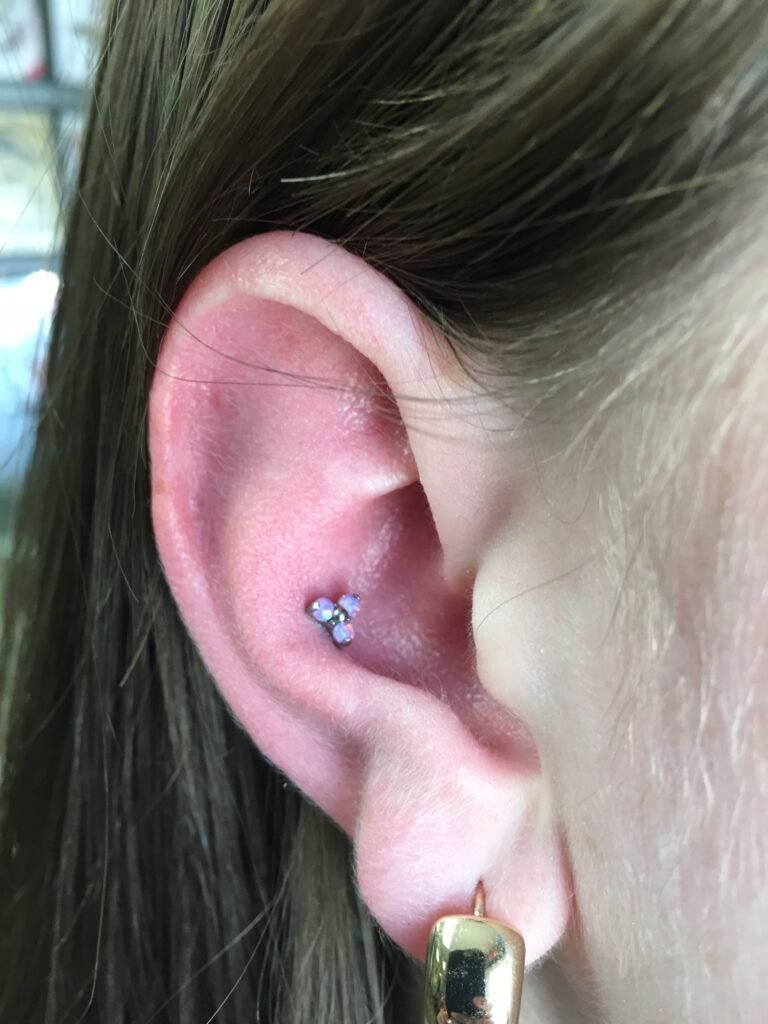A photo of a conch piercing. This is a type of ear piercing and is very popular among both men and women. The base jewelry is made of titanium and the toppers is a triple opal stone circle facets in the shape of a triangle. This piercing was done by Hope Boyd the body piercer at Near Me Tattoo at 6721 Bells Ferry Rd STE D110 Woodstock, Georgia 30189