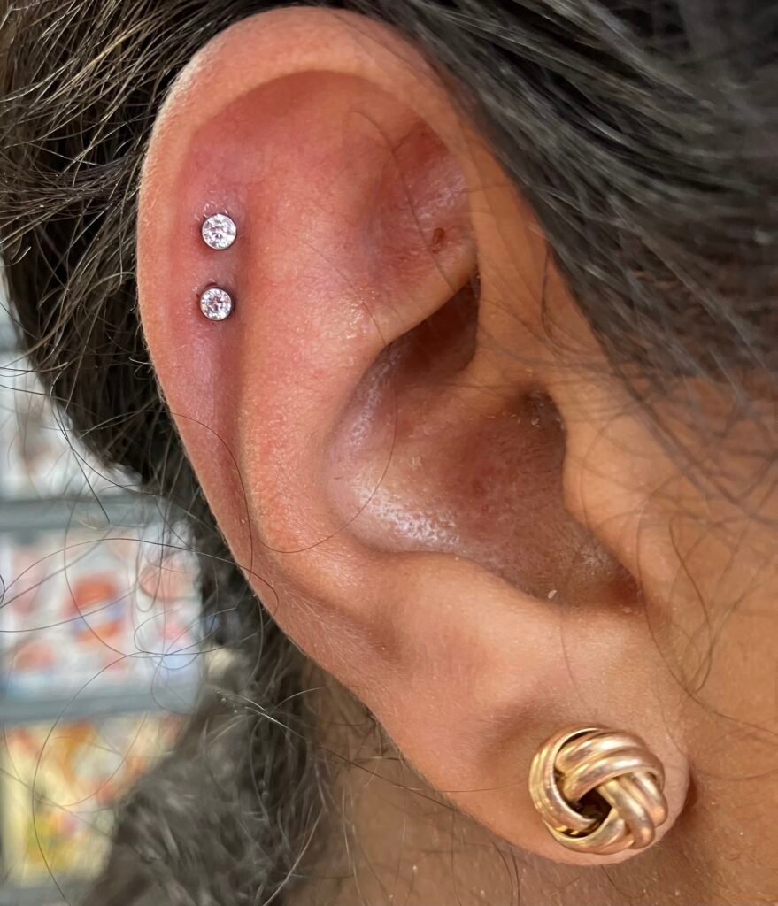 A beautiful double helix piercing on the ear of the wearer. This style of piercing is very popular for both men and women. The base of the jewelry used is titanium and the toppers on them are CZ stones. This piercing was done by Hope Boyd the body piercer at Near Me Tattoo at 6721 Bells Ferry Rd STE D110 Woodstock, Georgia 30189