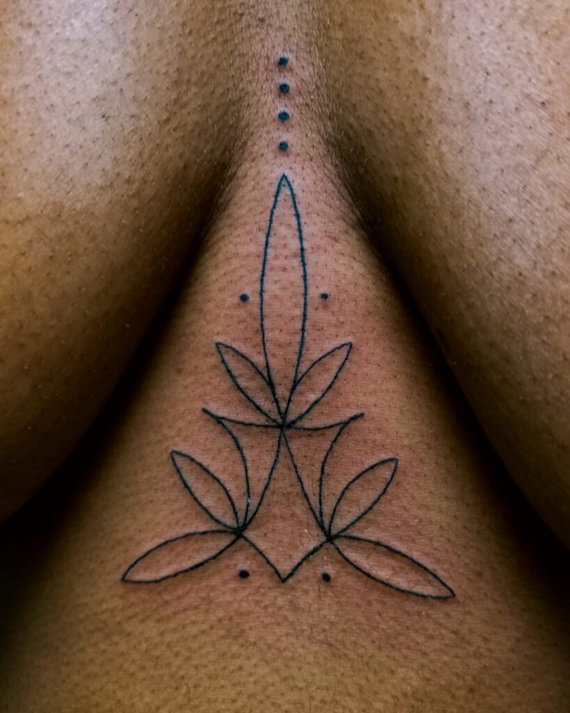 A fine line geometric sternum tattoo on a woman. It is a a triangular shaped design similar to pinstripe shapes on hot rods. It features looping and swirling thin lines and dots. It is very feminine and fits closely between the wearers breasts. This tattoo was made by Nathan Heinrich, co owner of Near Me Tattoo at 6721 Bells Ferry Rd Ste D110 Woodstock, Ga. 30189