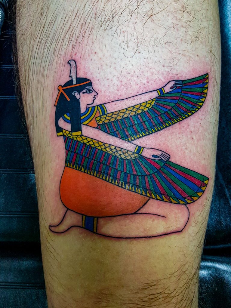 An illustrative color ink tattoo if the Egyptian Godess Maat. It is done with fine lines and traditional cultural colors found in ancient Egyptian artwork and styles. The tattoo is on the thigh of the wearer. This tattoo was made by Nathan Heinrich, co owner of Near Me Tattoo at 6721 Bells Ferry Rd Ste D110 Woodstock, Ga. 30189