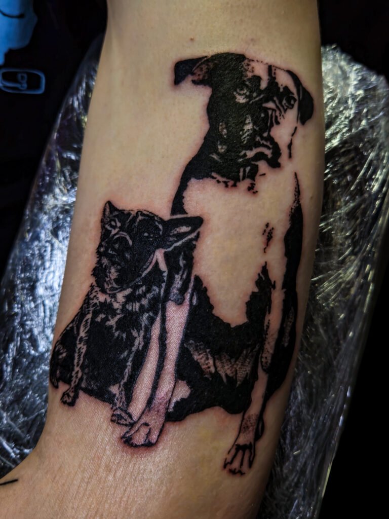 A tattoo of a semi realism blackwork silhouette pet portraits done in black ink. It features two of the clients childhood dogs that have passed. This is a memorial tattoo of a boxer dog and a Scottie type dog. This tattoo was made by Nathan Heinrich, co owner of Near Me Tattoo at 6721 Bells Ferry Rd Ste D110 Woodstock, Ga. 30189