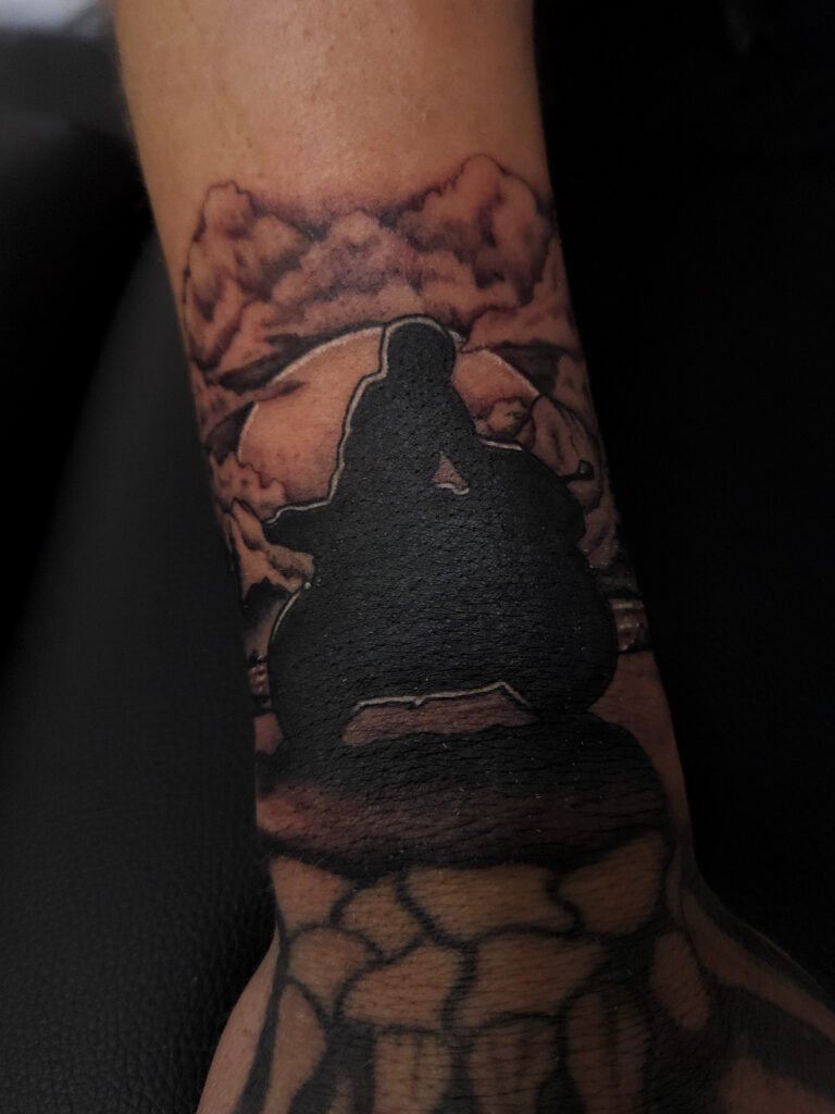 A black and grey or gray ink realism tattoo of a motorcycle rider. The rider and his sport bike is silhouetted on the wrist of the wearer above the hand and finger. in the background is a moonlit background with trees, mountains, clouds and a lake. This is the 2nd image. This tattoo was made by Nathan Heinrich, co owner of Near Me Tattoo at 6721 Bells Ferry Rd Ste D110 Woodstock, Ga. 30189