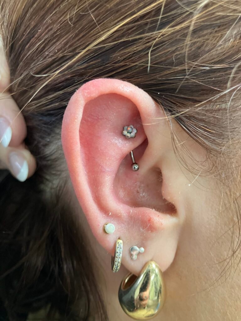 A picture of a rook piercing. This is a very popular ear piercing for both men and women. The jewelry used is made of titanium and the topper on the jewelry is made of a faux opal stone. This piercing was done by Hope Boyd the body piercer at Near Me Tattoo at 6721 Bells Ferry Rd STE D110 Woodstock, Georgia 30189