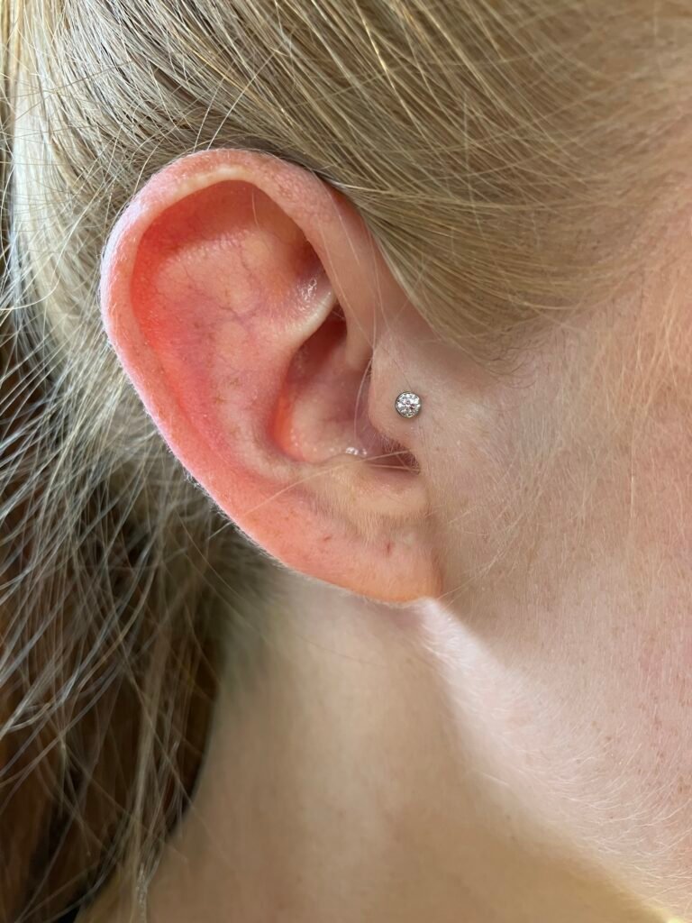 A photograph of a tragus piercing. It is done on the ear of a woman. This is also a popular piercing for men as well. The jewelry used is titanium with a single CZ stone topper. This piercing was done by Hope Boyd the body piercer at Near Me Tattoo at 6721 Bells Ferry Rd STE D110 Woodstock, Georgia 30189