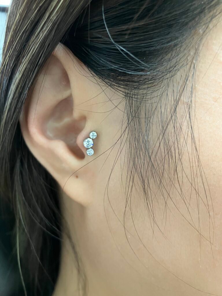 A photograph of a beautifully done tragus ear piercing. The jewelry is very femenine and is a very popular piercing for woman and men to get. The jewelry is made of titanium and the topper is made from a triple cz stone pattern. This piercing was done by Hope Boyd the body piercer at Near Me Tattoo at 6721 Bells Ferry Rd STE D110 Woodstock, Georgia 30189
