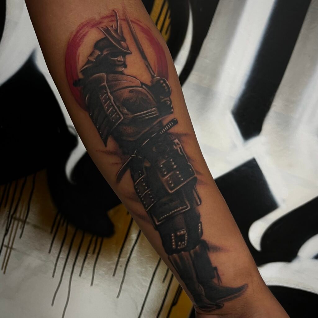 A blackwork with red accent tattoo depicting a Japanese samurai in full battle armor and in his hand holding a katana sword. He is done with heavy black shading which gives him the aura of a dark knight. In the background of the image is a Japanese enso symbol mimicking like it was done in a brush style. This tattoo was done by Josh Davies at Near Me Tattoo at 6721 Bells Ferry Rd STE D110 Woodstock Georgia 30189