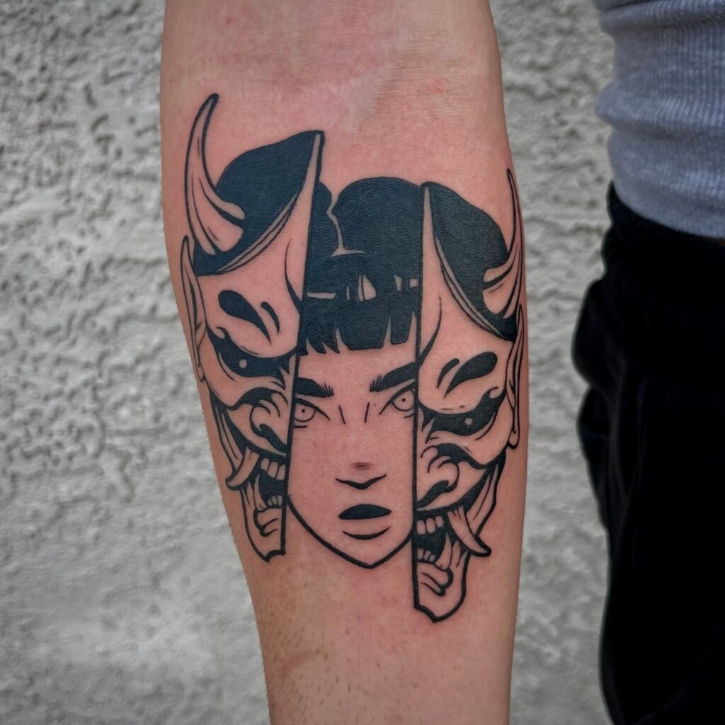 A blackwork illustrative tattoo design on the forearm of the wearer showing a split Japanese Hanya mask with a woman’s face behind it. It is done completely with black ink creating heavy contrast from the skin. This tattoo was done by Josh Davies at Near Me Tattoo at 6721 Bells Ferry Rd STE D110 Woodstock Georgia 30189