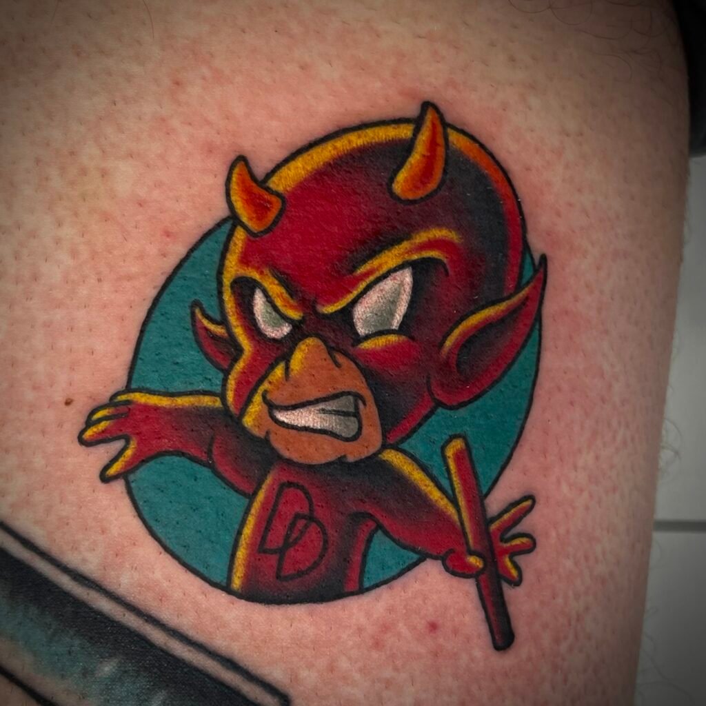 A new school or Neo American traditional kewpie version of the Marvel superhero Dare Devil. It shows a colorful cartoon character coming out of a blue ink circle that contrasts perfectly with the bold red color of the super hero’s costume. In the hand of the character is his iconic staff weapon. This tattoo was done by Josh Davies at Near Me Tattoo at 6721 Bells Ferry Rd STE D110 Woodstock Georgia 30189